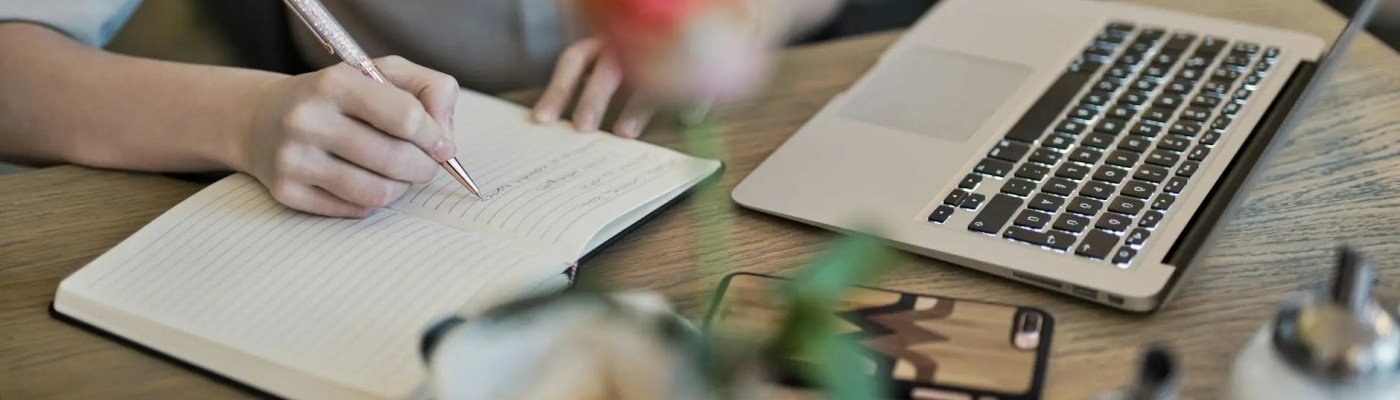 person writing on a notebook beside macbook